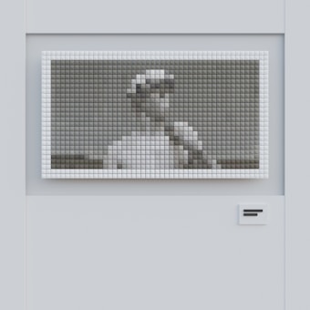 A grayscale pixelated image is displayed on a wall, showing what appears to be a person wearing a hat. The picture is made up of evenly spaced square tiles, creating a mosaic effect. The wall is smooth and light-colored with a small rectangular detail positioned near the bottom.