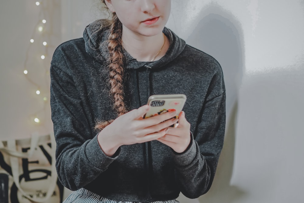 Femme en pull noir tenant un smartphone blanc