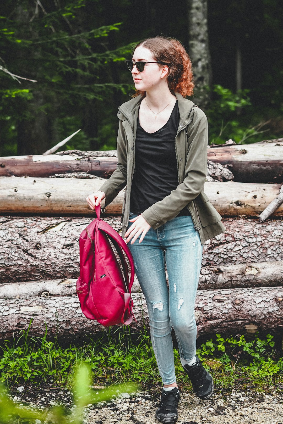 woman in green jacket and blue denim jeans holding red leather handbag