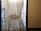 A white curtain tied with a bow partially covers a window, allowing some light to filter through. The outside view shows a metal staircase and urban building backdrop. The setting has a minimalistic and domestic feel, with the curtain framing the window strongly.