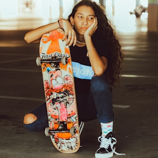woman in blue tank top holding orange and black skateboard