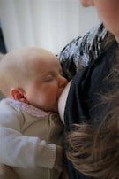 A baby is breastfeeding, nestled against a person wearing a patterned garment. The baby appears peaceful and content.