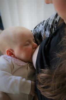 A baby is breastfeeding, nestled against a person wearing a patterned garment. The baby appears peaceful and content.