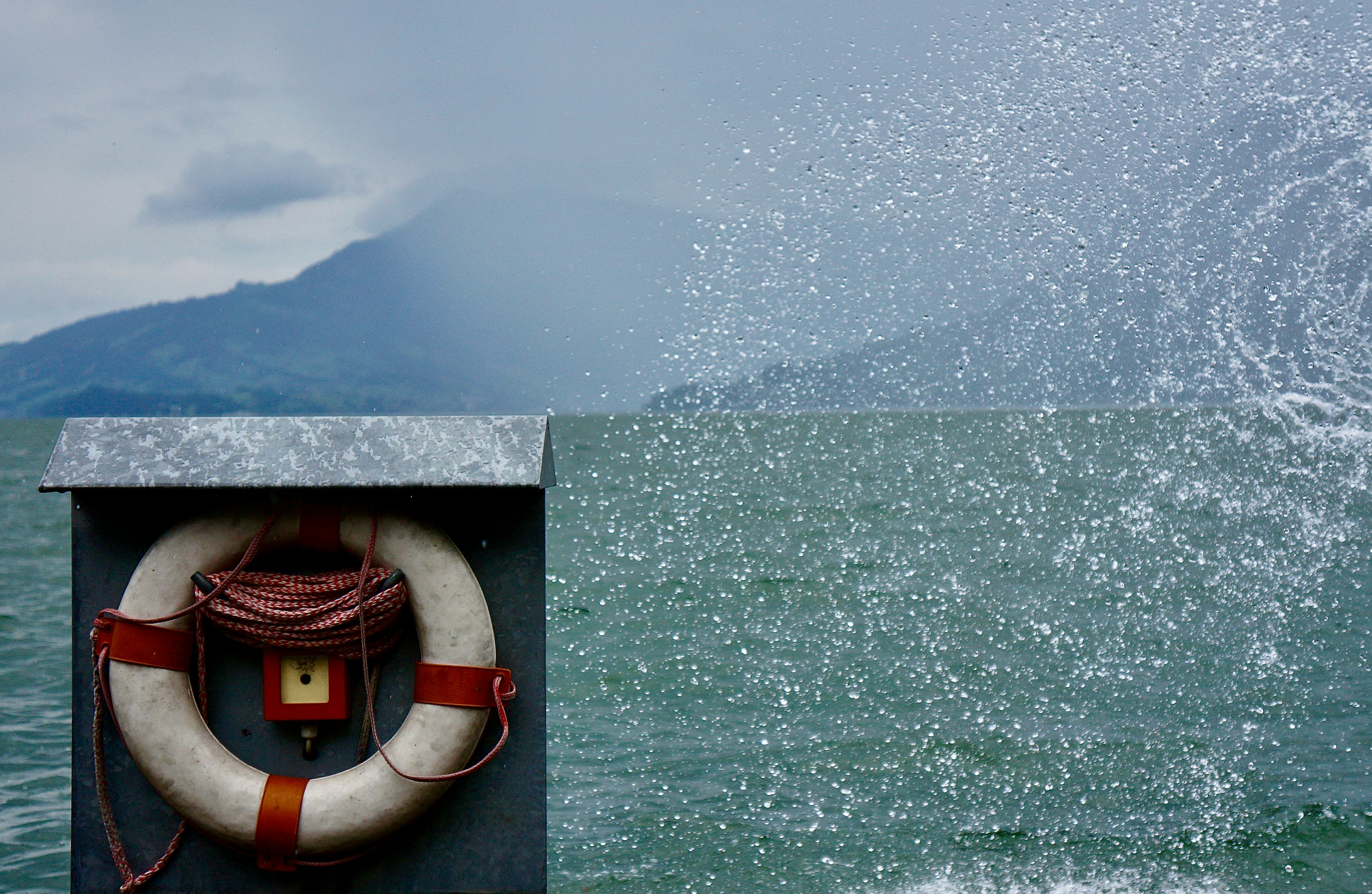 A body of water with a spray from a wave, a mountain in the background, and a life preserver in the foreground.