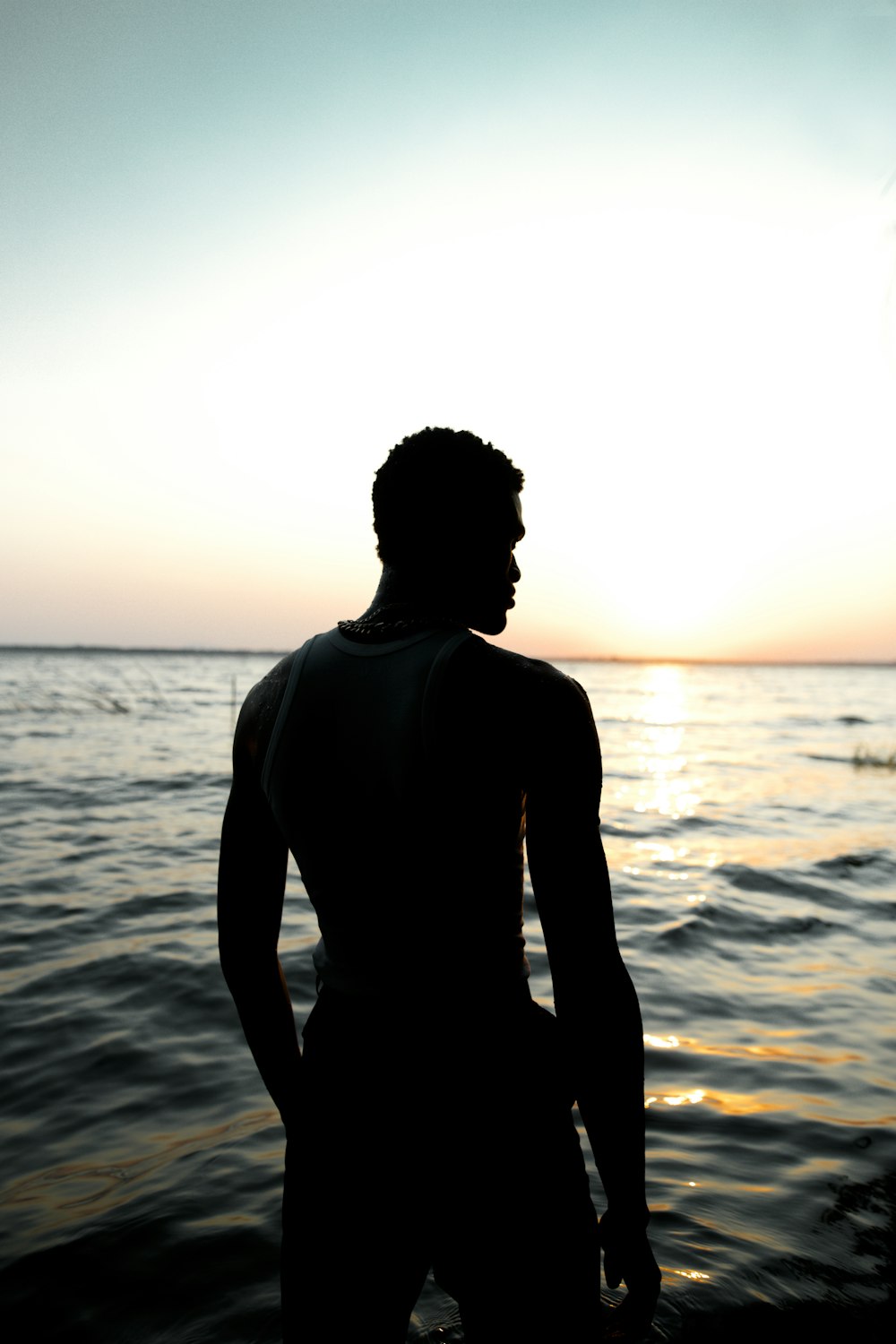 uomo in camicia nera a maniche lunghe in piedi in riva al mare durante il giorno