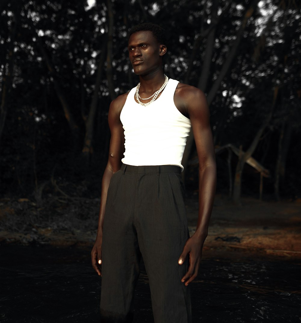 man in white tank top and gray pants standing on dirt ground