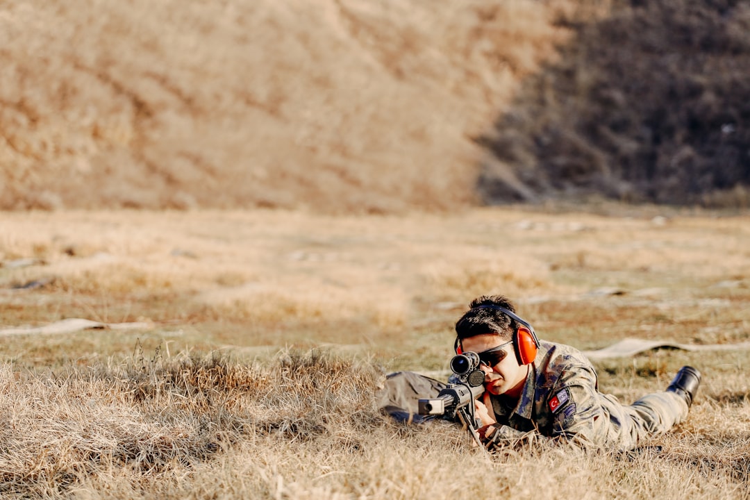 man in black and gray camouflage jacket sitting on brown grass field during daytime