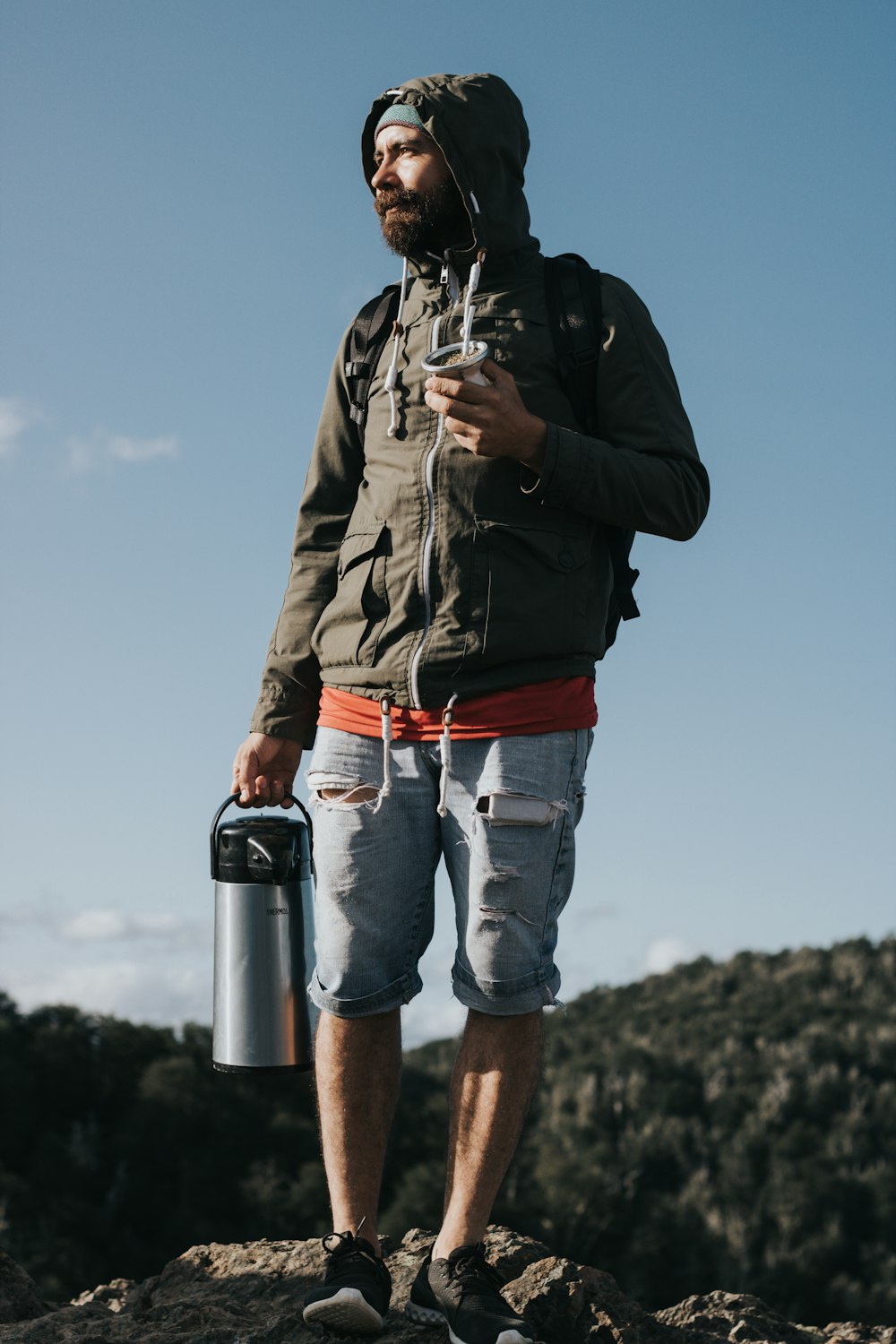 man in black jacket and blue denim shorts holding black and silver camera