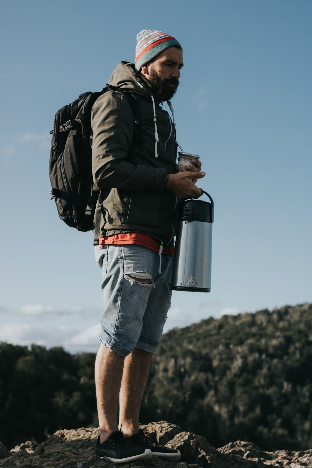 man in black jacket and blue denim shorts carrying black and gray travel mug