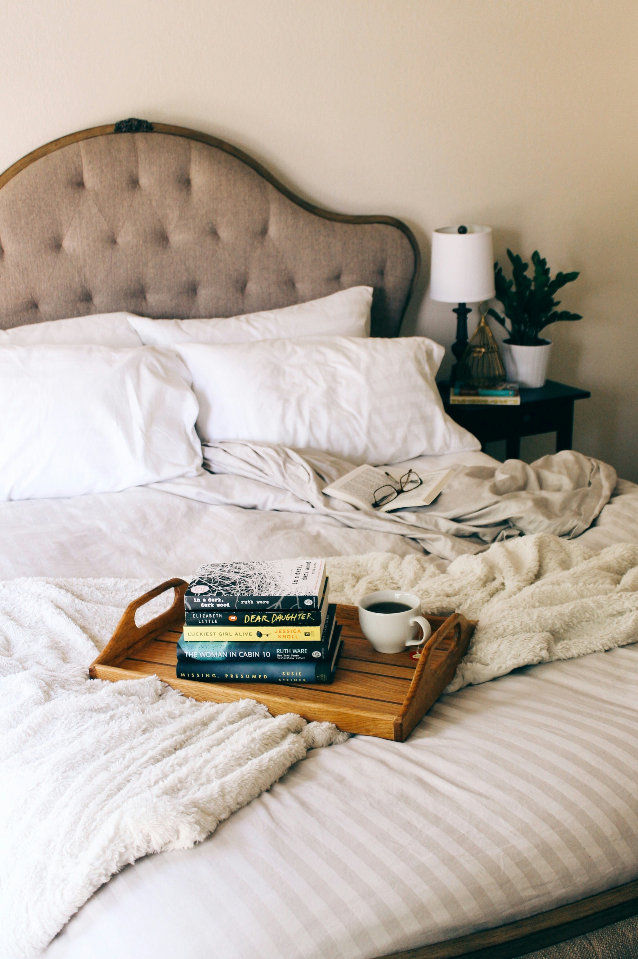 white bed linen with books stacked on top of a brown wooden tray