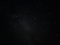 A dark night sky sprinkled with numerous small, bright stars. There are areas of varying darkness, suggesting the presence of distant nebulae.