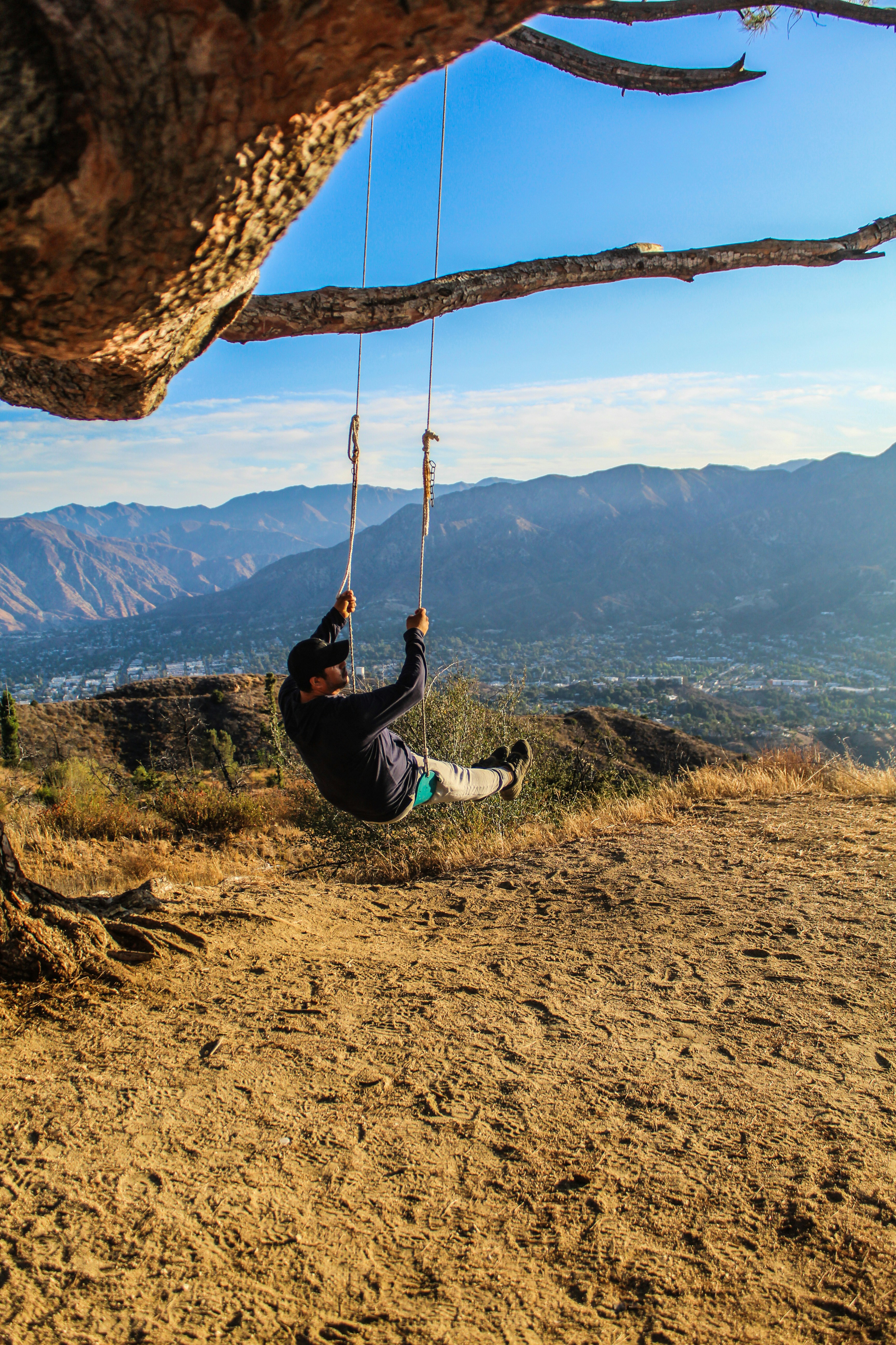 man in black jacket and blue denim jeans sitting on swing during daytime