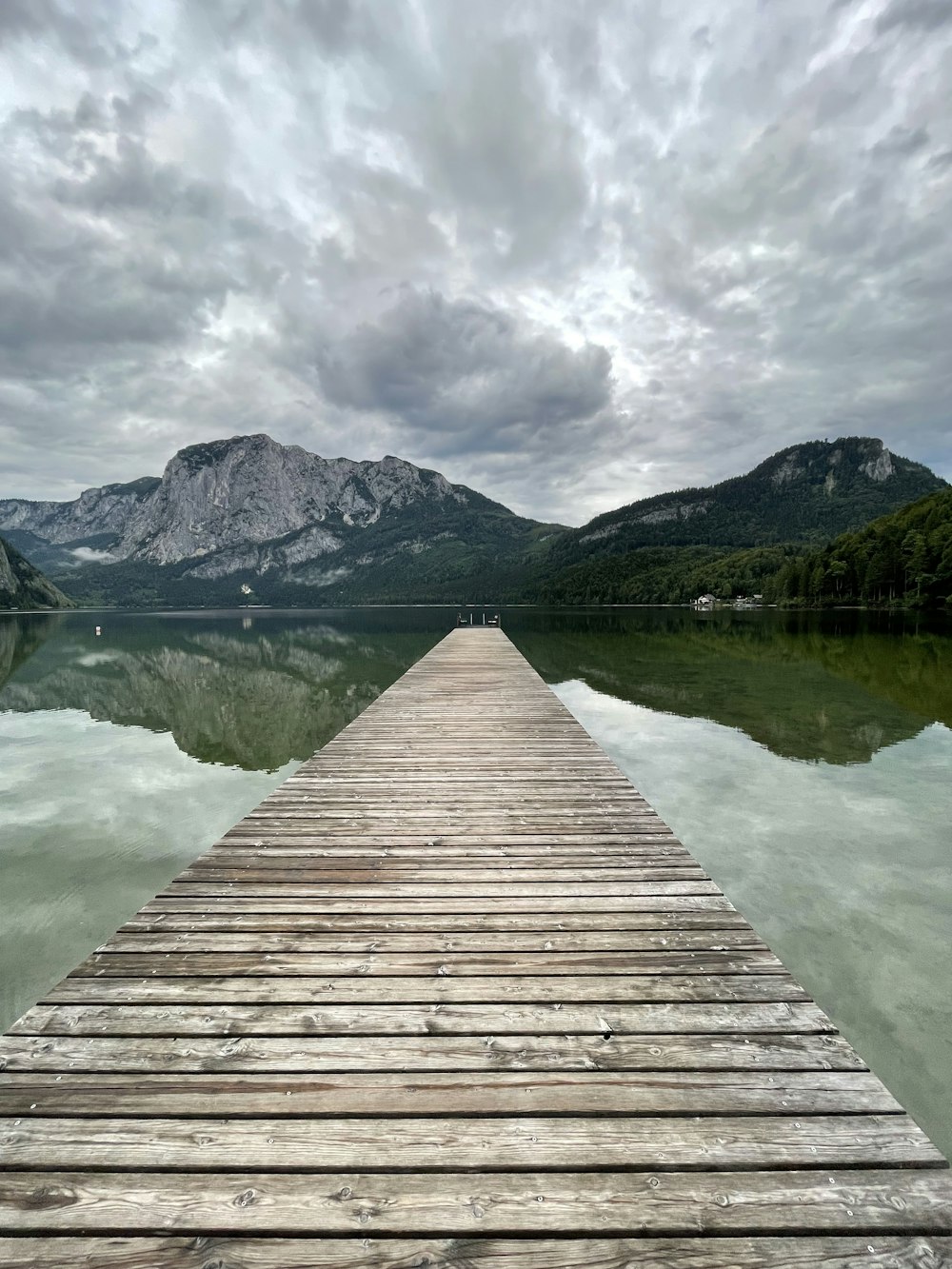 brown wooden dock on lake near mountain under cloudy sky during daytime