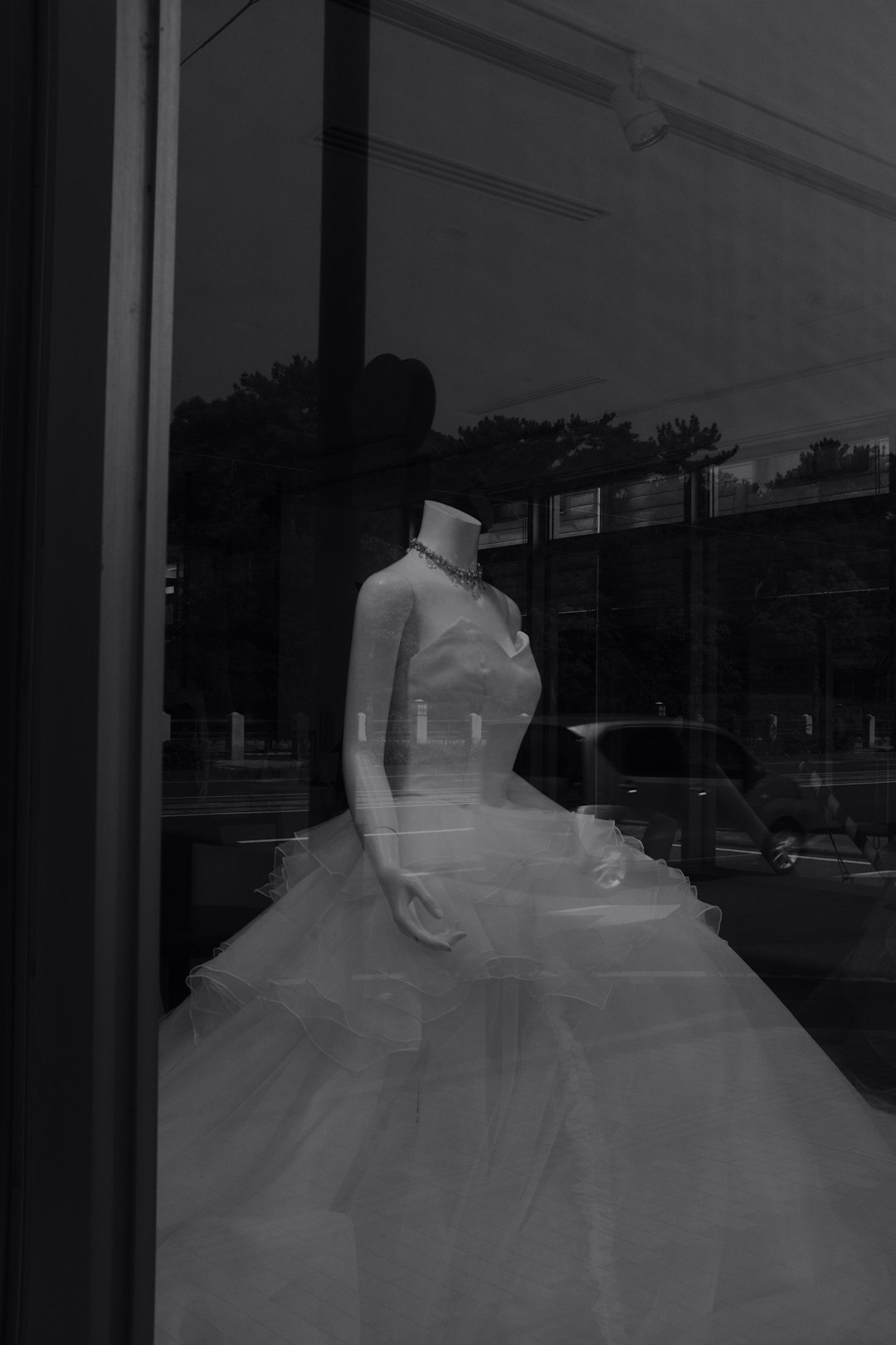 grayscale photo of bride and groom standing near glass window
