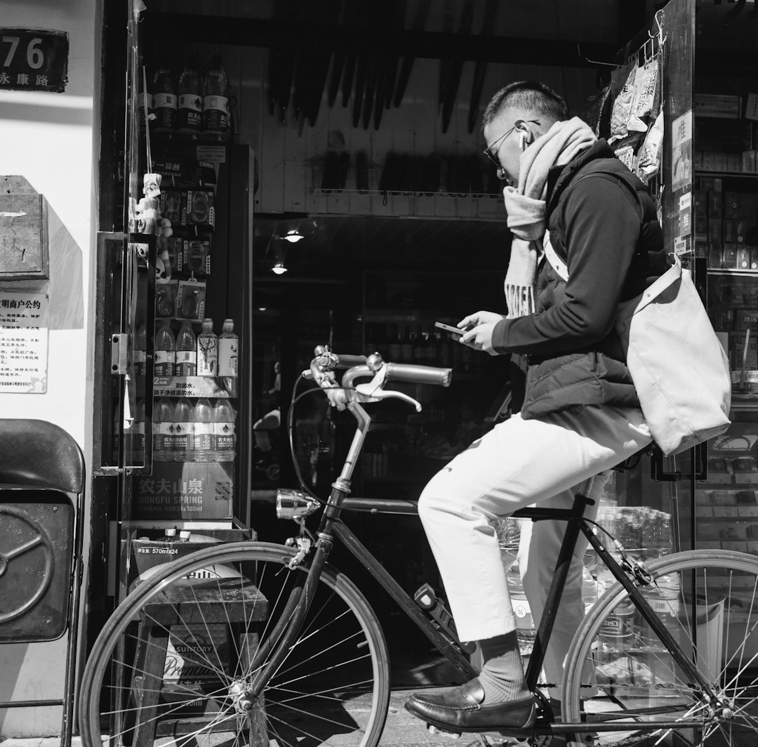 man in black jacket and white pants riding on bicycle in grayscale photography