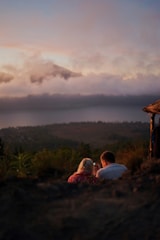 couple sitting on ground near brown wooden house during daytime