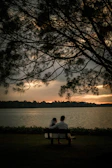 A serene couple seated on a rustic bench, bathed in charcoal-gray twilight, sharing a quiet moment.
