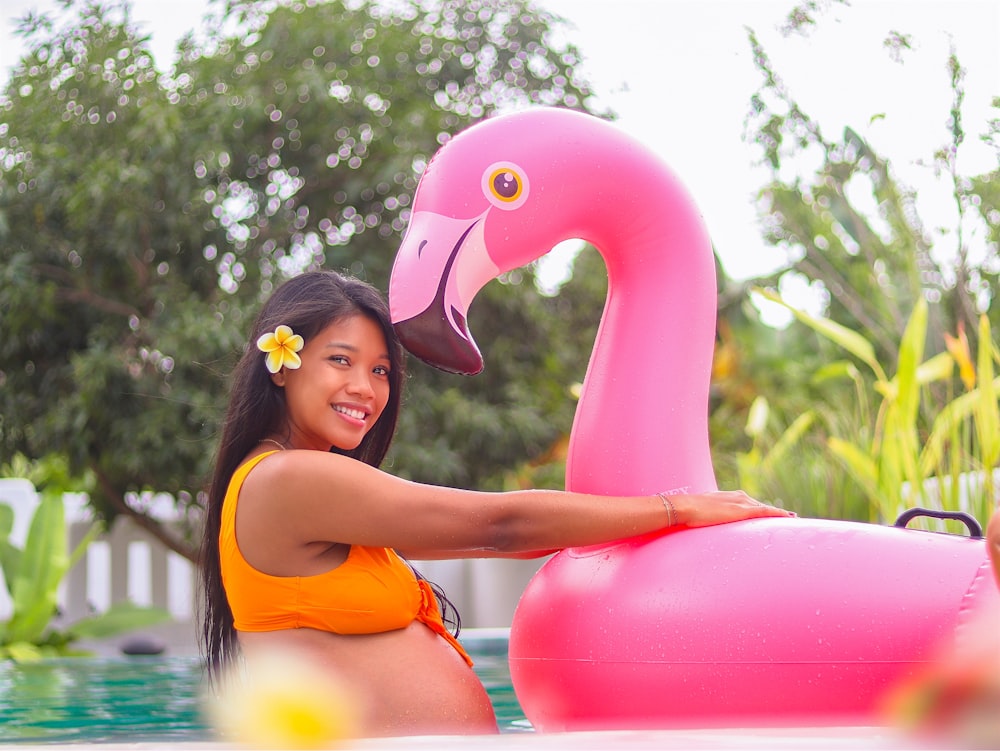 Frau im orangefarbenen Bikinioberteil mit rosa aufblasbarem Flamingo