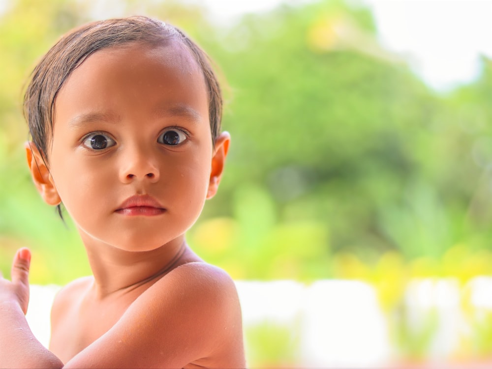 topless boy standing near green grass during daytime