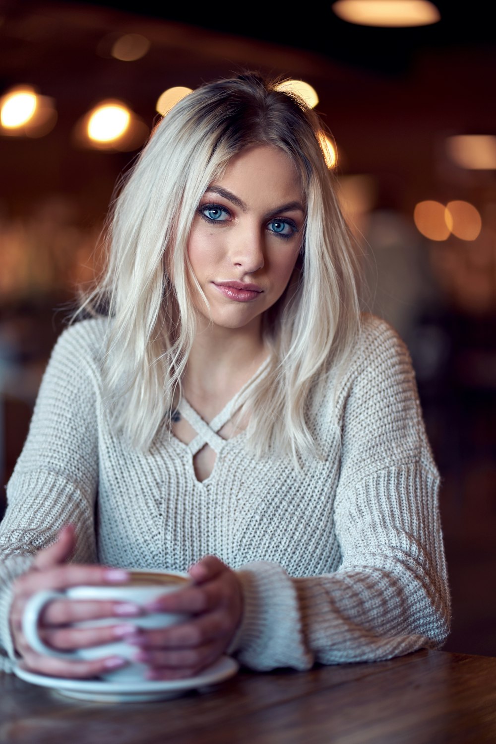 woman in white knit sweater holding white ceramic mug