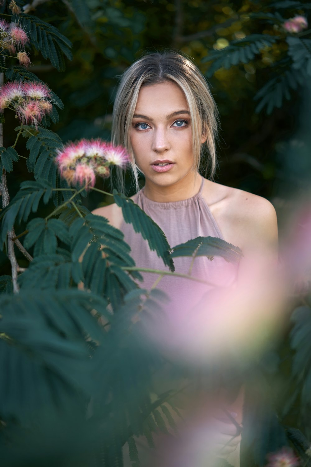 woman in white tank top standing beside purple flowers