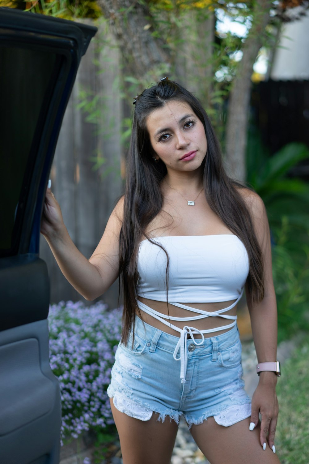 woman in white tank top and blue denim shorts standing beside car door during daytime