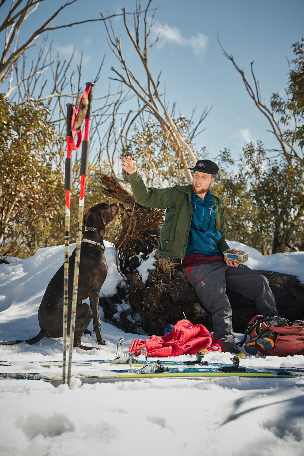 man in blue jacket and black pants sitting on red and white snow covered ground beside