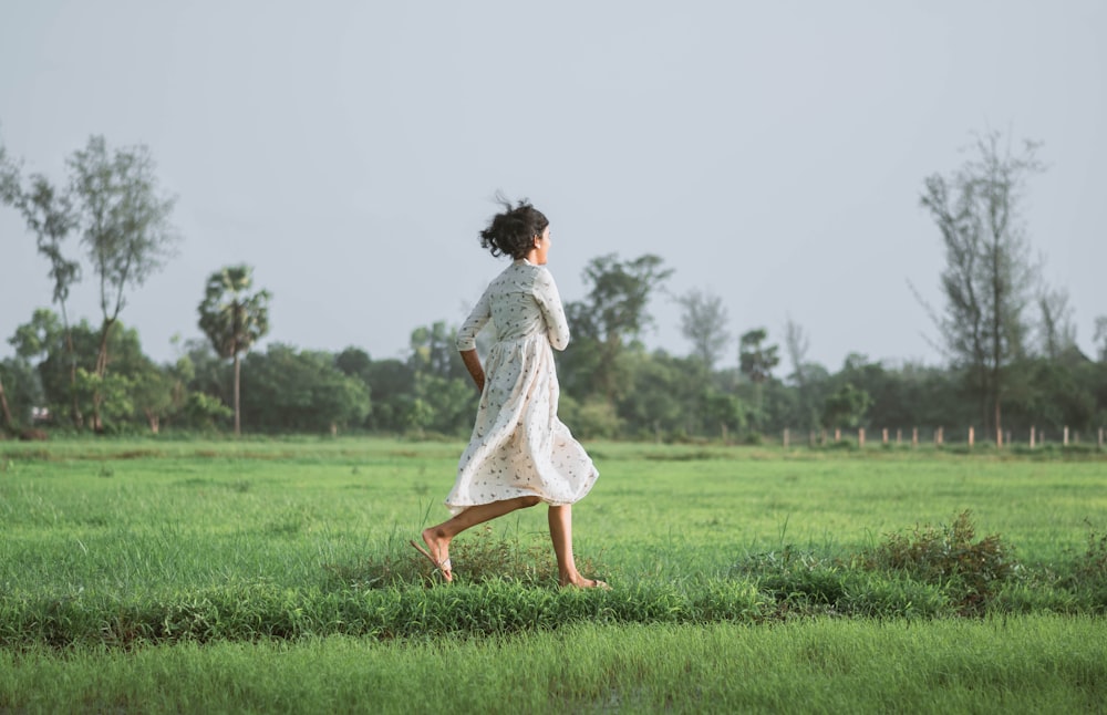 woman in white dress walking on green grass field during daytime