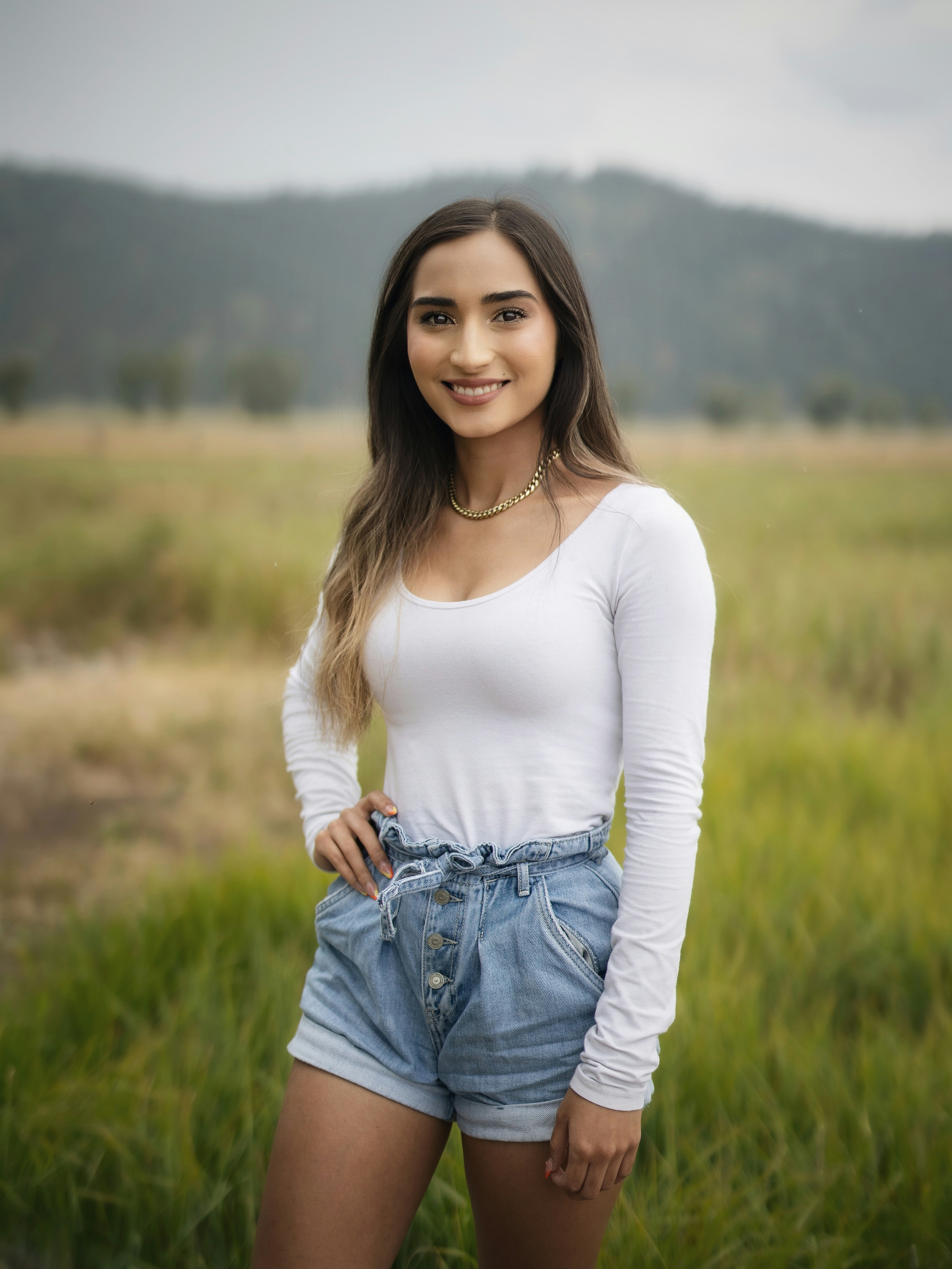 mujer en camisa blanca de manga larga y pantalones cortos de mezclilla azul de pie en el campo de hierba verde durante