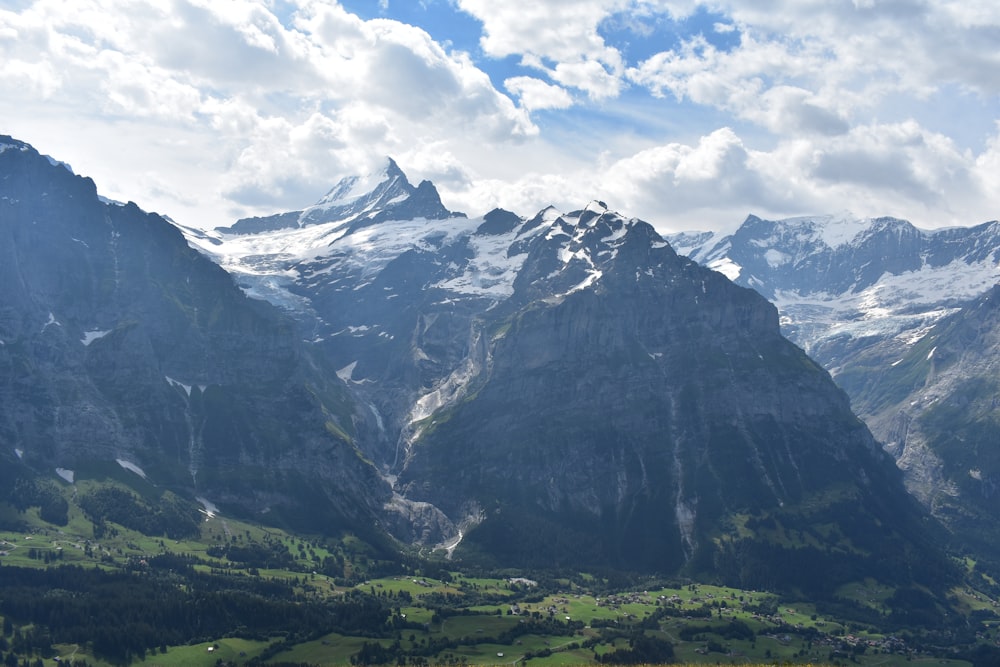 green grass field near snow covered mountain under white clouds and blue sky during daytime