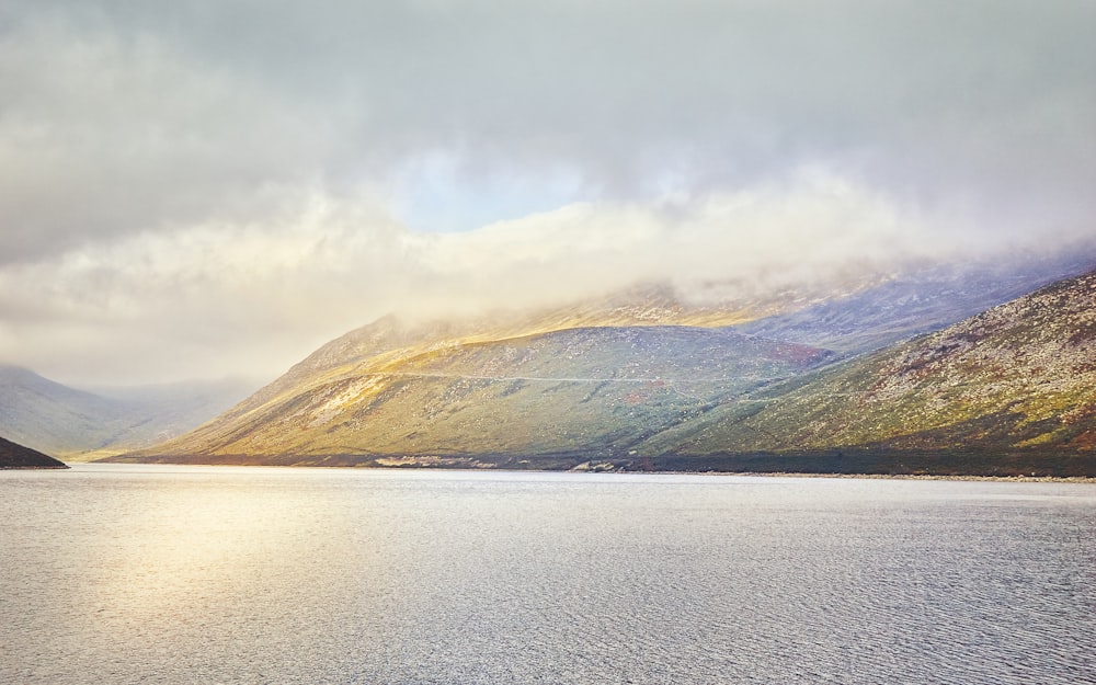 brown and green mountains beside body of water under white clouds during daytime