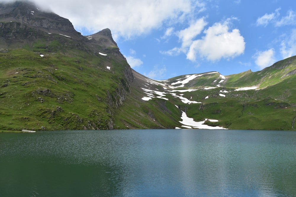 montanhas verdes e brancas ao lado do lago sob o céu azul durante o dia