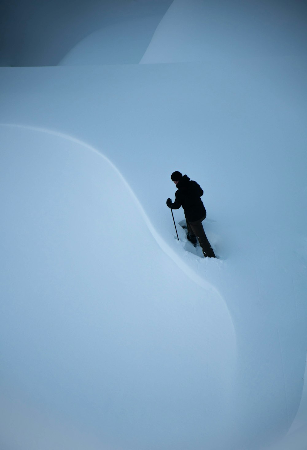 Hombre con chaqueta y pantalones negros caminando sobre el suelo cubierto de nieve durante el día