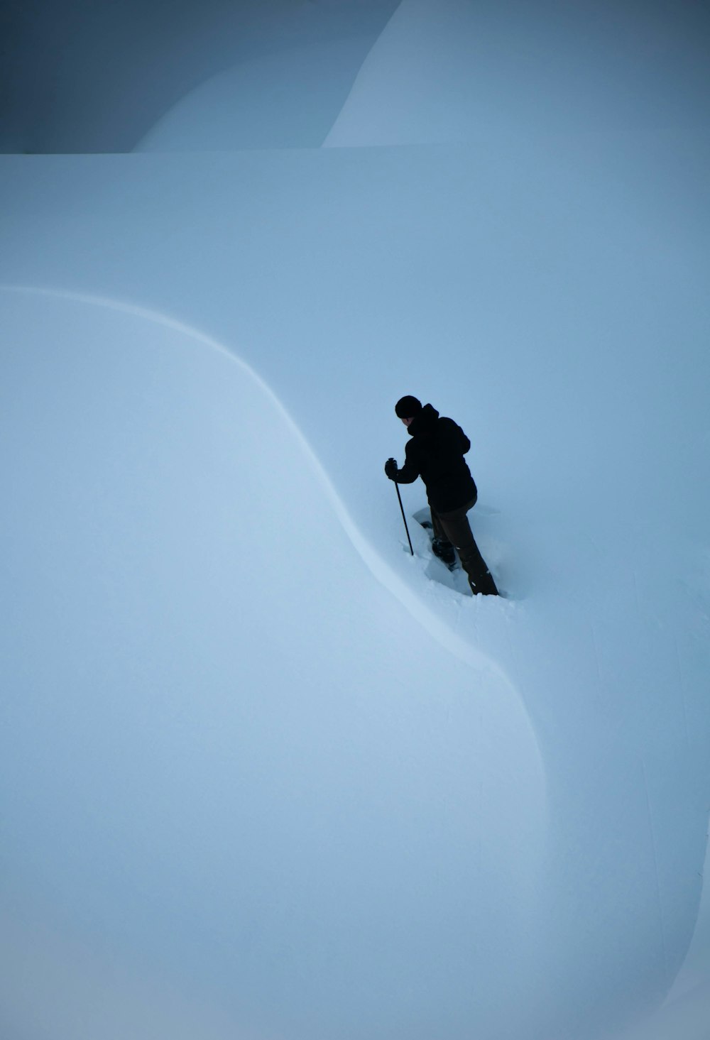 uomo in giacca e pantaloni neri che camminano su terreno coperto di neve durante il giorno