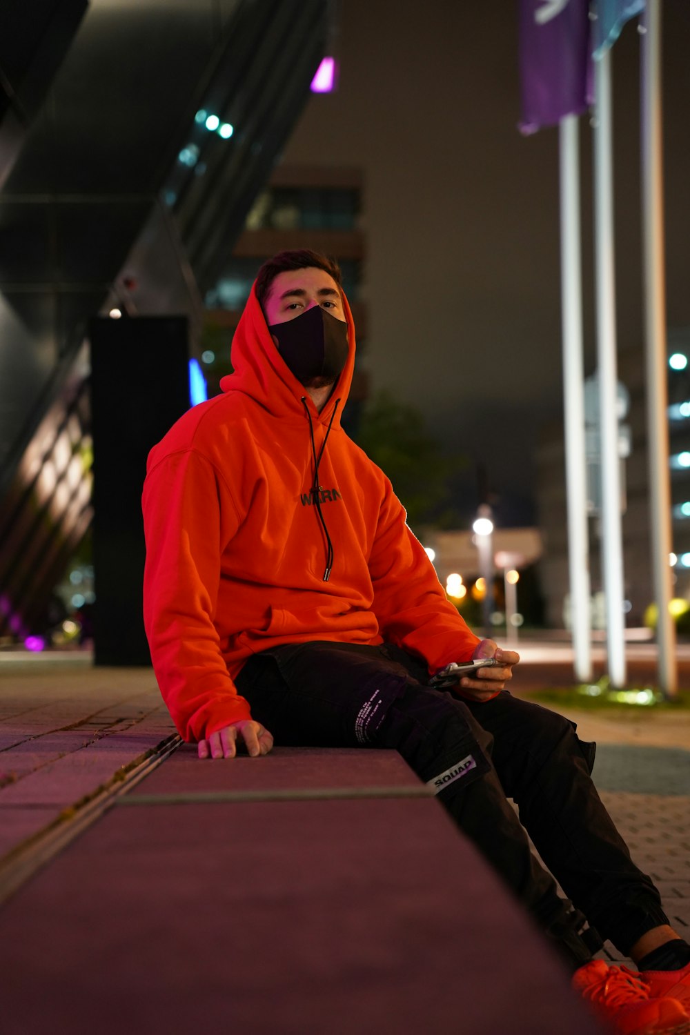 man in orange hoodie sitting on brown wooden floor