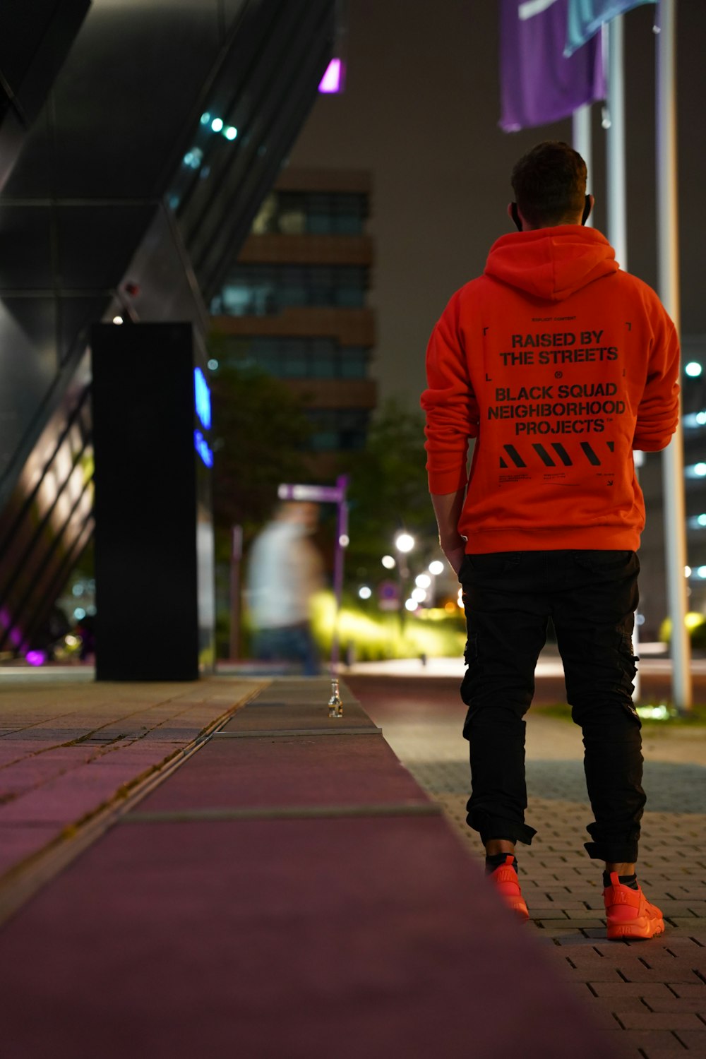 man in red hoodie standing on sidewalk during night time