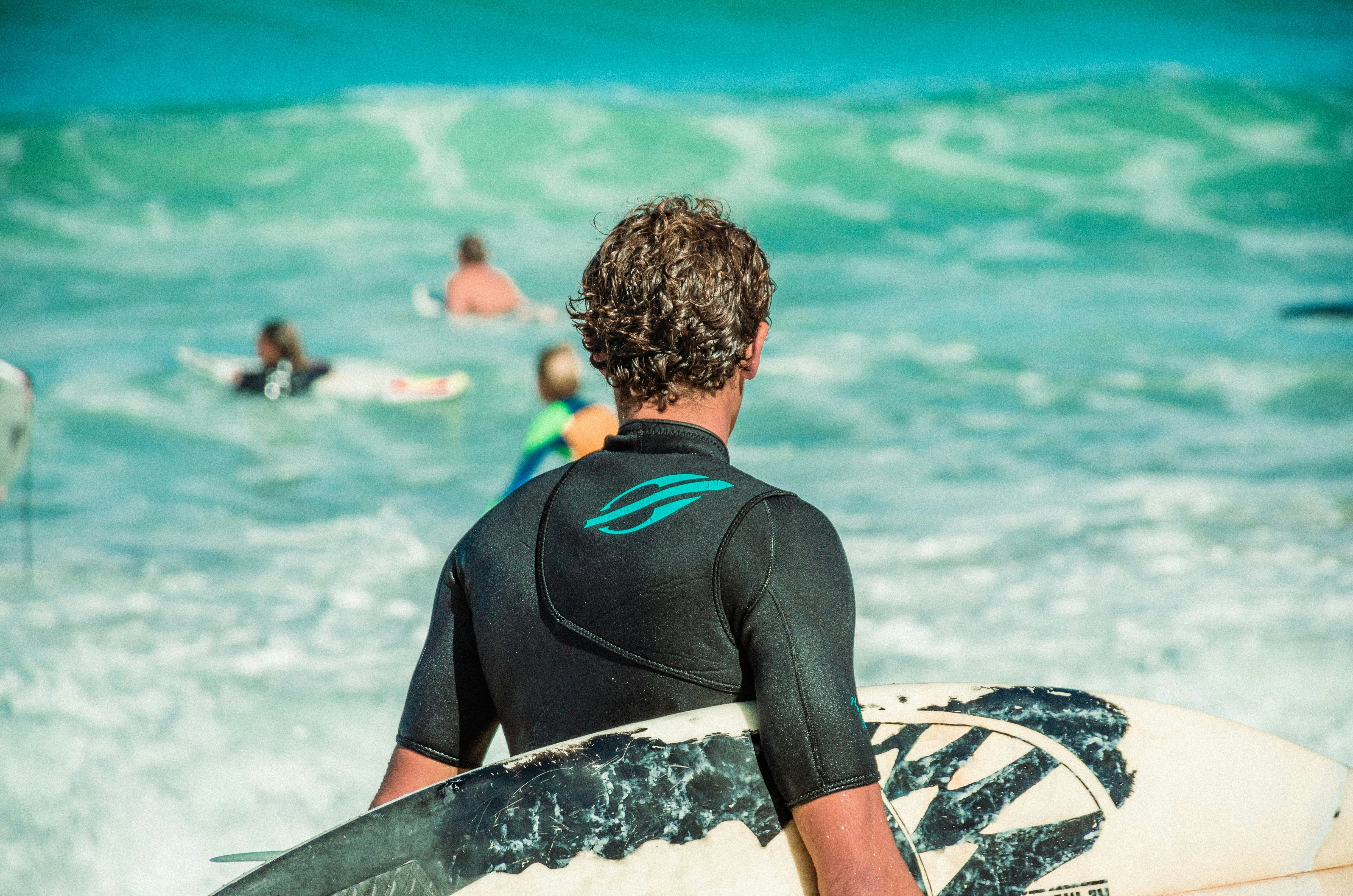 man in black wet suit sitting on black and white surfboard on beach during daytime