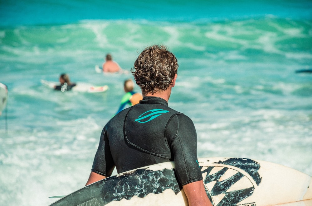 hombre en traje de neopreno negro sentado en una tabla de surf en blanco y negro en la playa durante el día