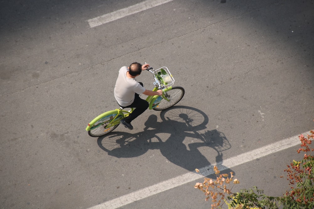 man in white t-shirt riding on green bicycle on gray asphalt road during daytime