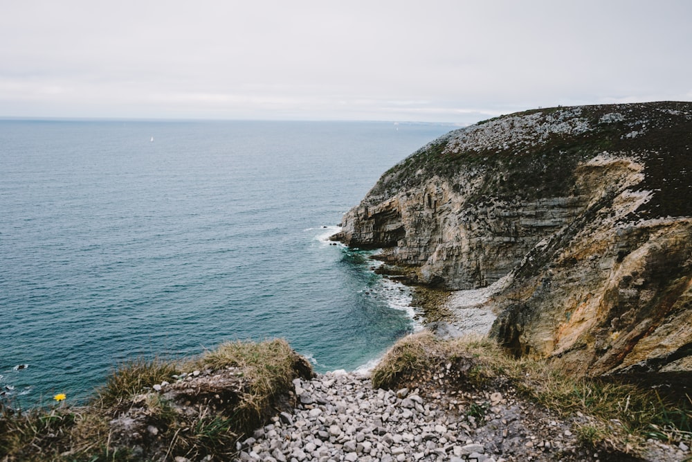 gray rocky mountain beside blue sea under white sky during daytime