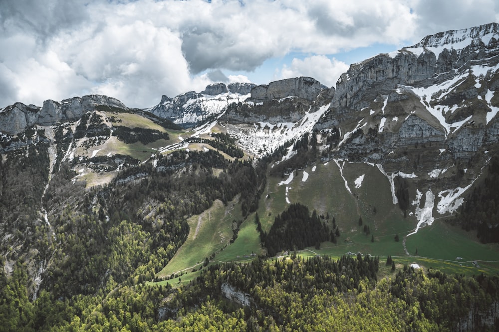 green grass field near mountain under white clouds during daytime