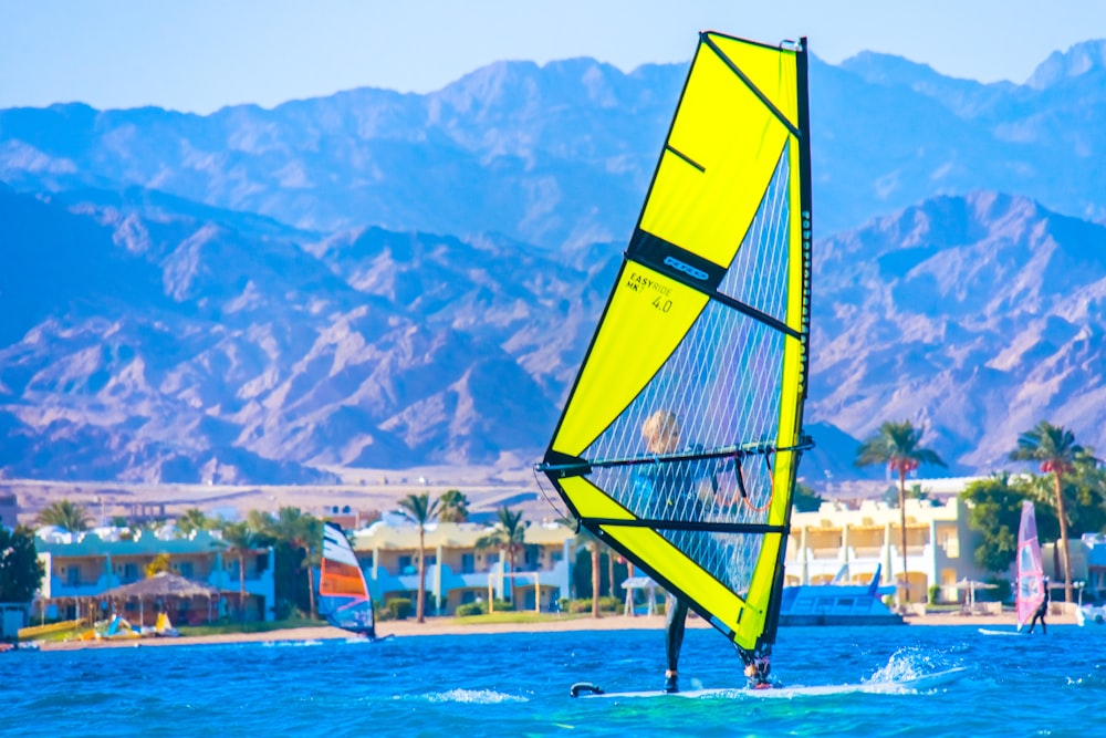 yellow and blue sail boat on water near mountain during daytime