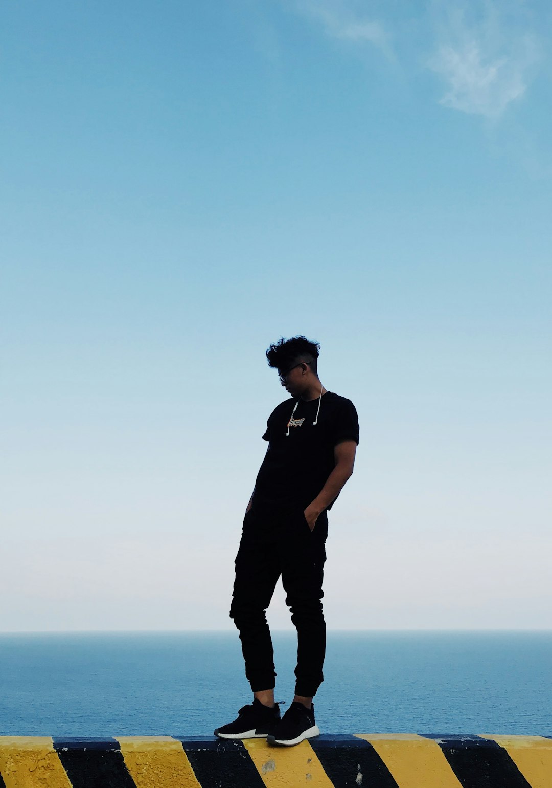 man in black tank top and black pants standing on the seashore during daytime