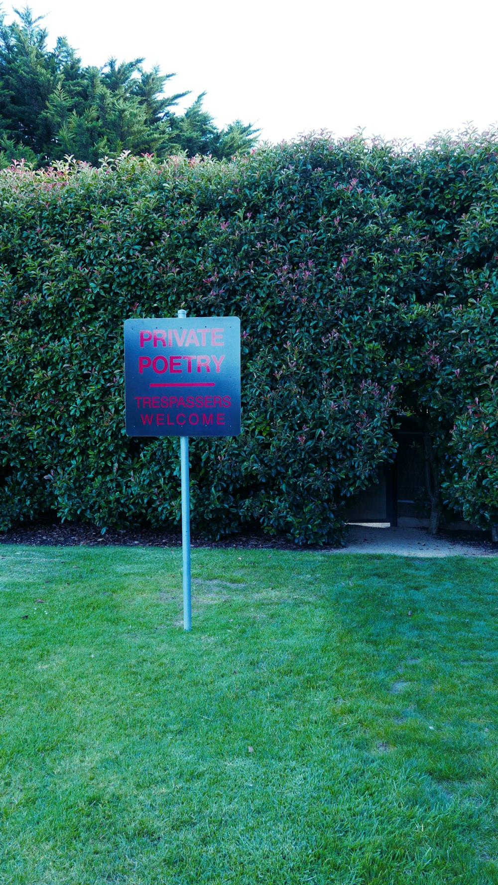 a sign that is in the grass near a hedge