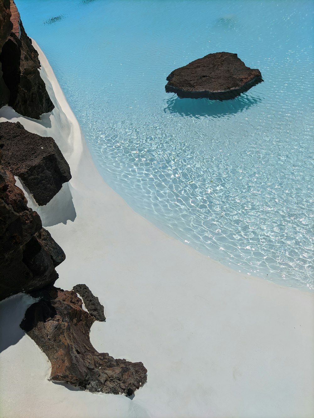 brown rock formation on white sand beach