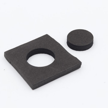 A black rectangular foam piece with a circular cut-out alongside a separate circular foam piece. The rectangular piece appears to be the source of the circular piece.