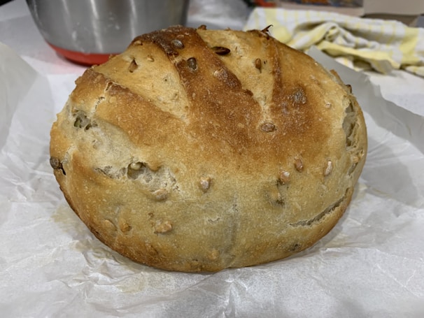 A rustic loaf of bread with a golden crust, resting beside a bowl of seeds