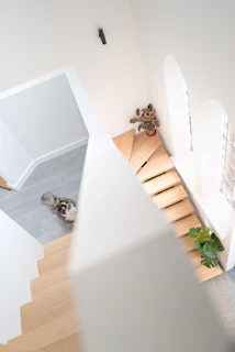 A multi-level cat playground featuring natural wood and soft pastel fabrics, designed to fit under a modern staircase.