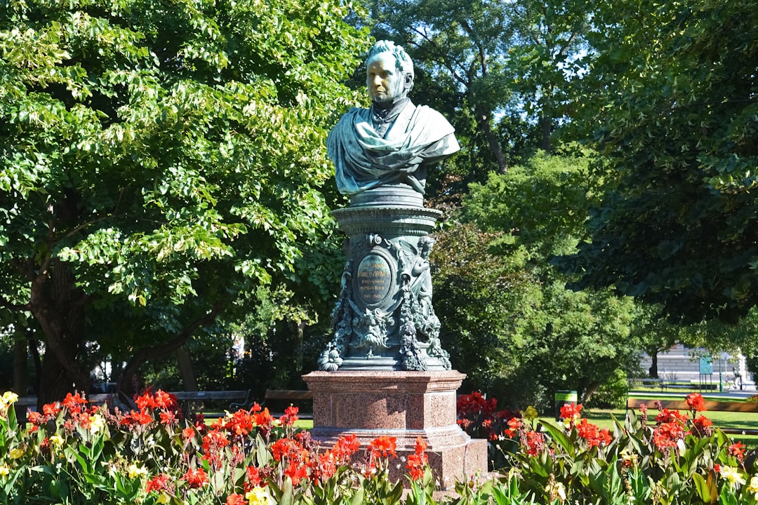 statue of man surrounded by red flowers and green trees during daytime