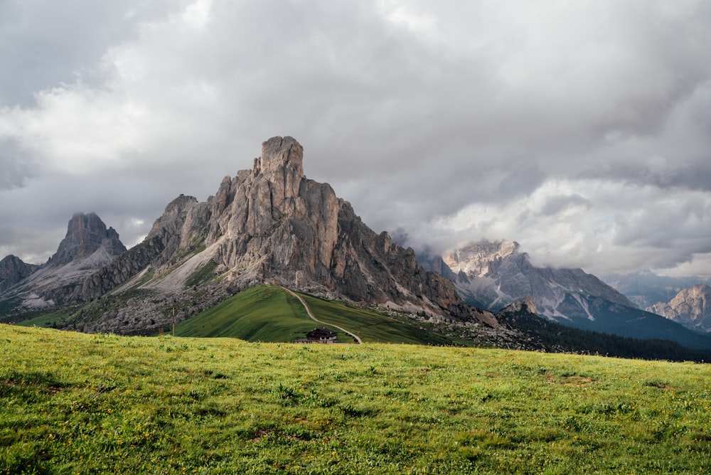 green grass field near rocky mountain under white cloudy sky during daytime